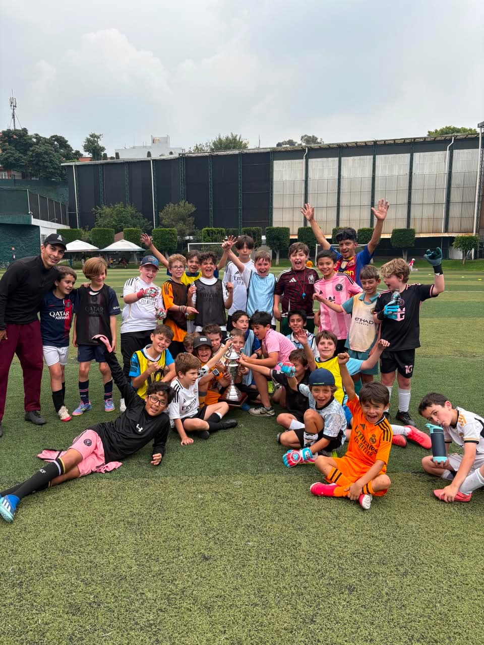 Grupo de niños del Curso de Verano Falcons celebrando con el trofeo en la cancha